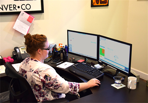 L&L Glass employee sitting at a desk in front of two monitors and a keyboard in the scheduling phase of our process for installation.