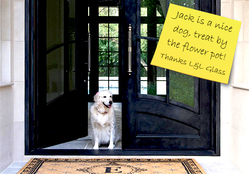 Front entry of a house and one of the double doors is open. A white Golden Retriever sits in the doorway. There is a note on the door, "Jack is a nice dog, treat by the flower pot!" Thanks L&L Glass 